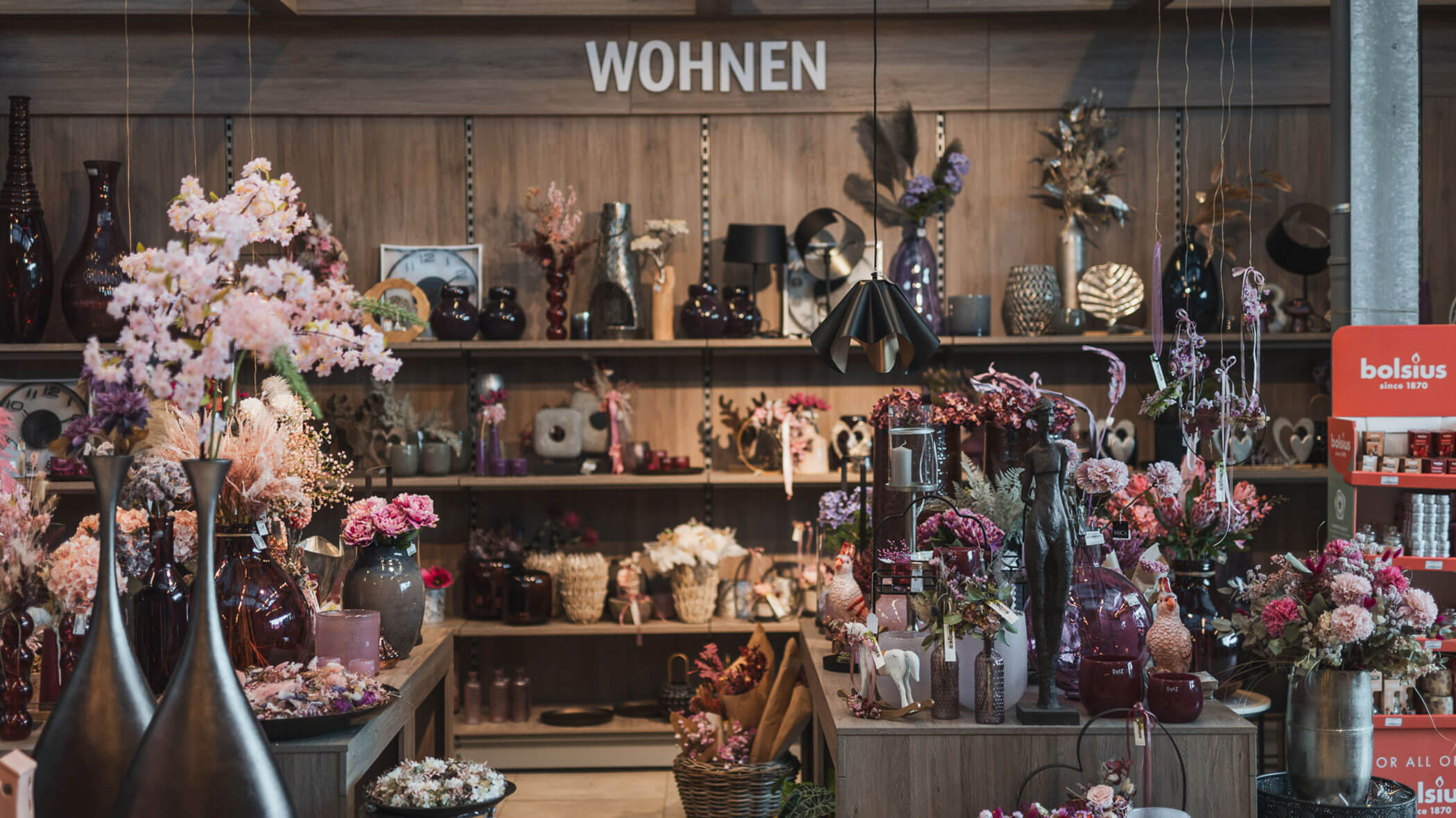 Ladeneinrichtung mit Regalen mit dekorativen Blumen, Vasen und Wohndekoration unter einem Schild mit der Aufschrift WOHNEN. - Obojes