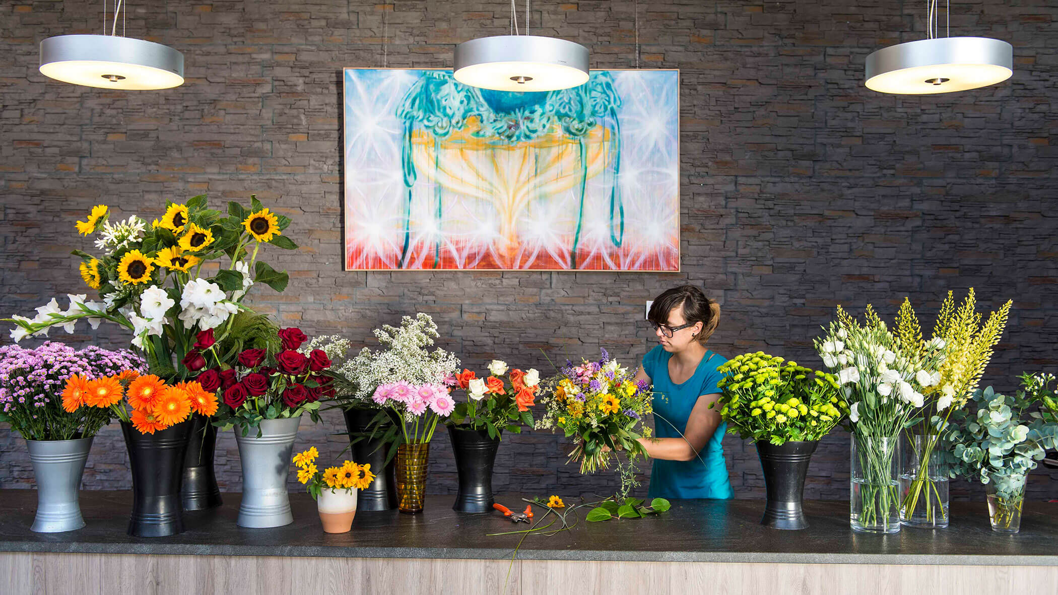 Eine Floristin arrangiert hinter einem Tresen einen Blumenstrauß mit verschiedenen bunten Blumen in Vasen. - Obojes