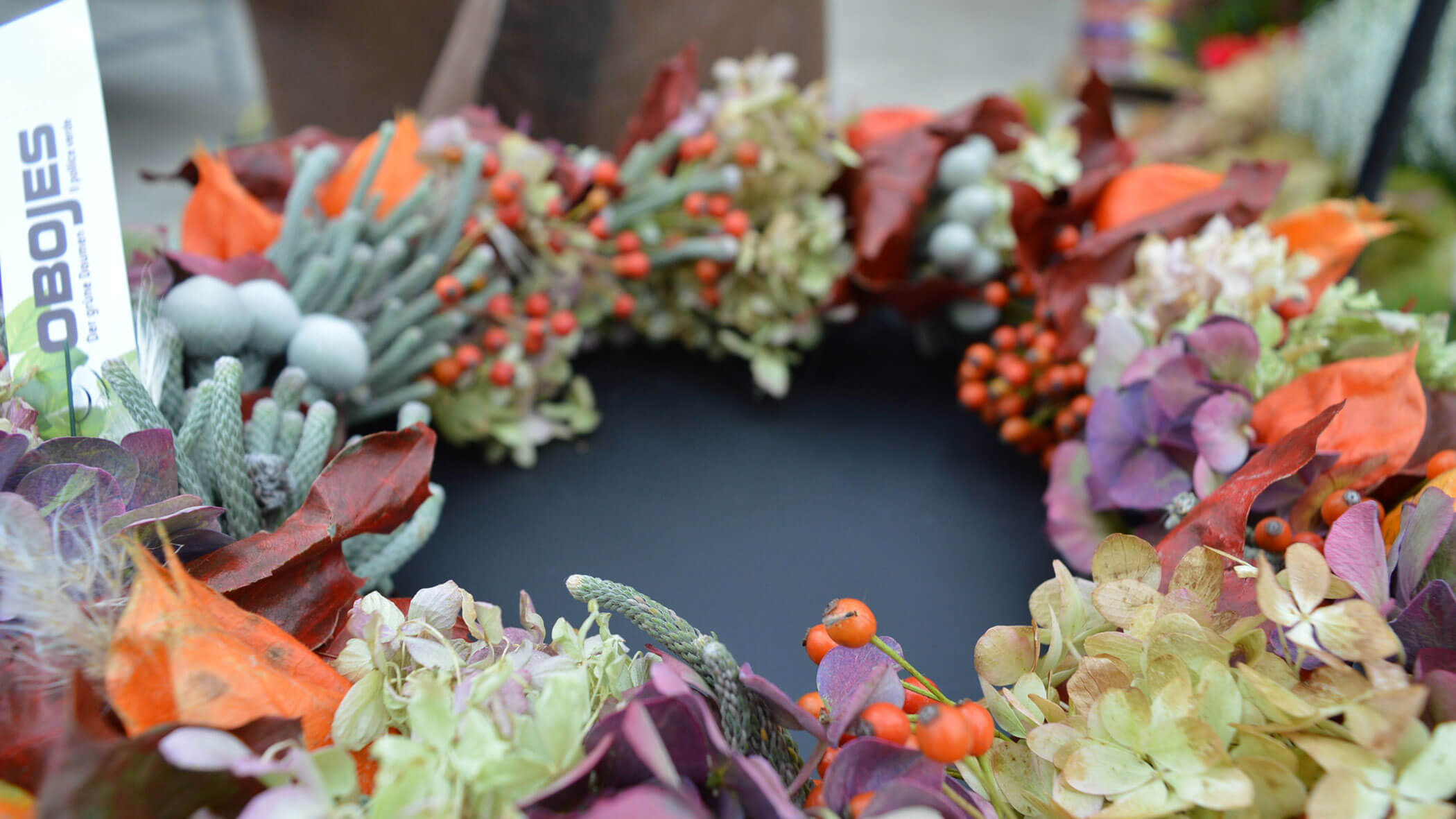 Ein farbenfroher Herbstkranz mit Beeren, Trockenblumen und Blättern auf einer schwarzen Oberfläche. - Obojes