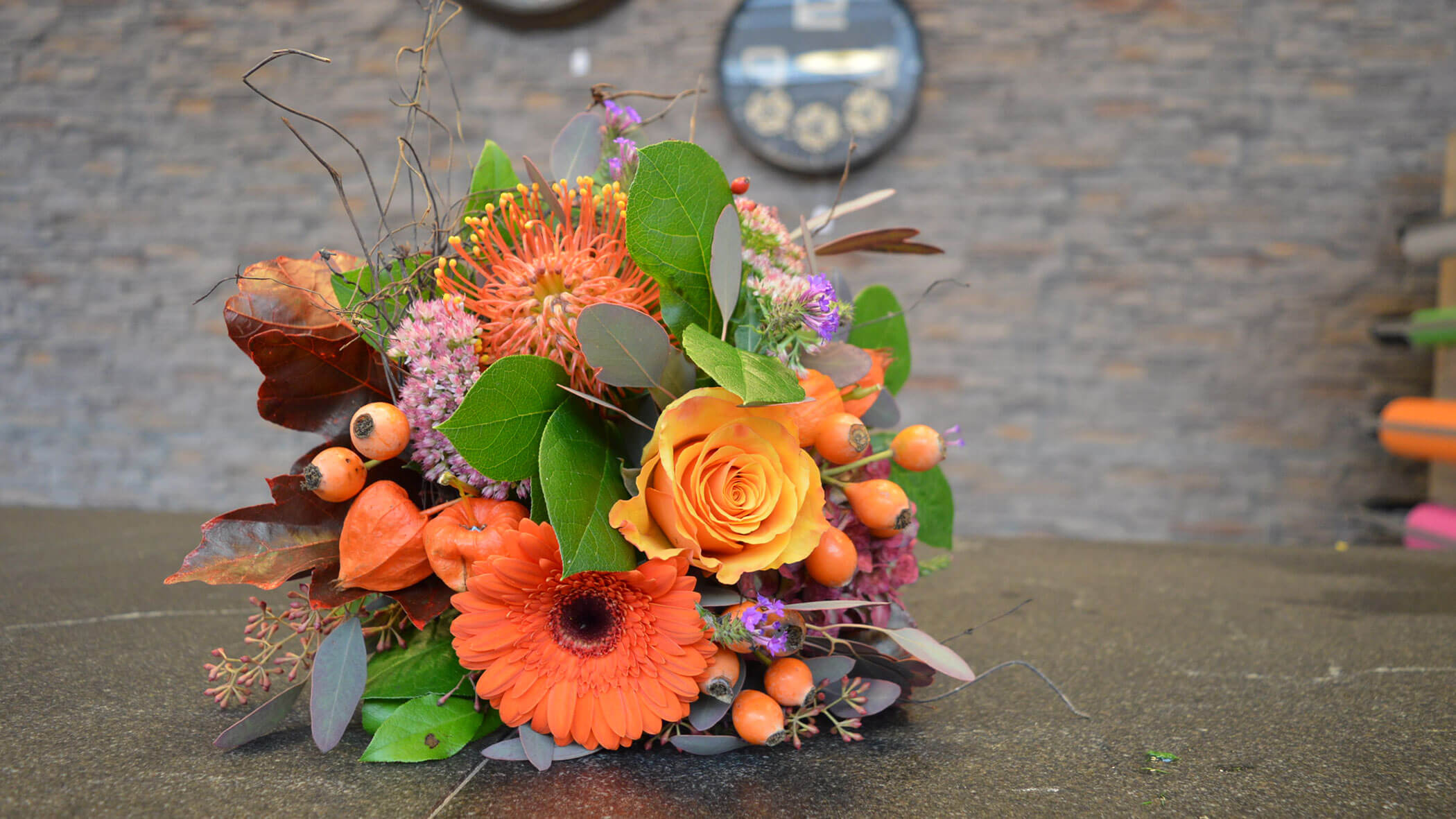 Orange und gelber Blumenstrauß mit grünen Blättern und Beeren auf einer dunklen Oberfläche, Steinwand Hintergrund. - Obojes