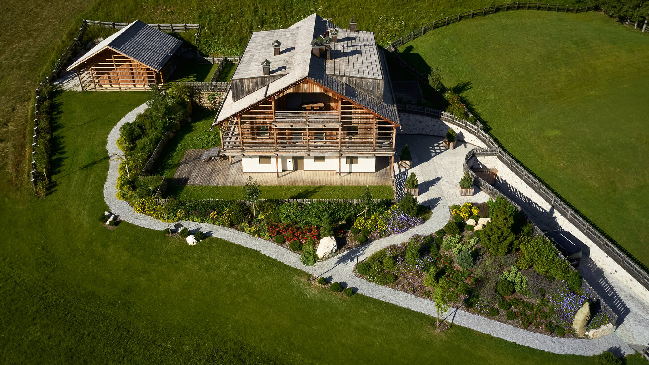 Luftaufnahme eines Hauses im Chalet-Stil mit Garten und Steinweg, umgeben von grünem Rasen und einem Zaun. - Obojes