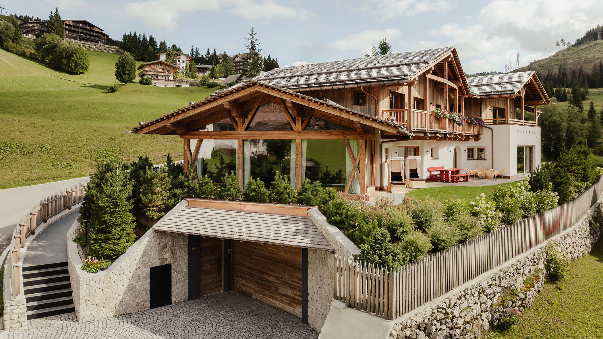 Ein Holz- und Steinchalet mit Garten, auf einem grünen Hügel unter einem teilweise bewölkten Himmel gelegen. - Obojes