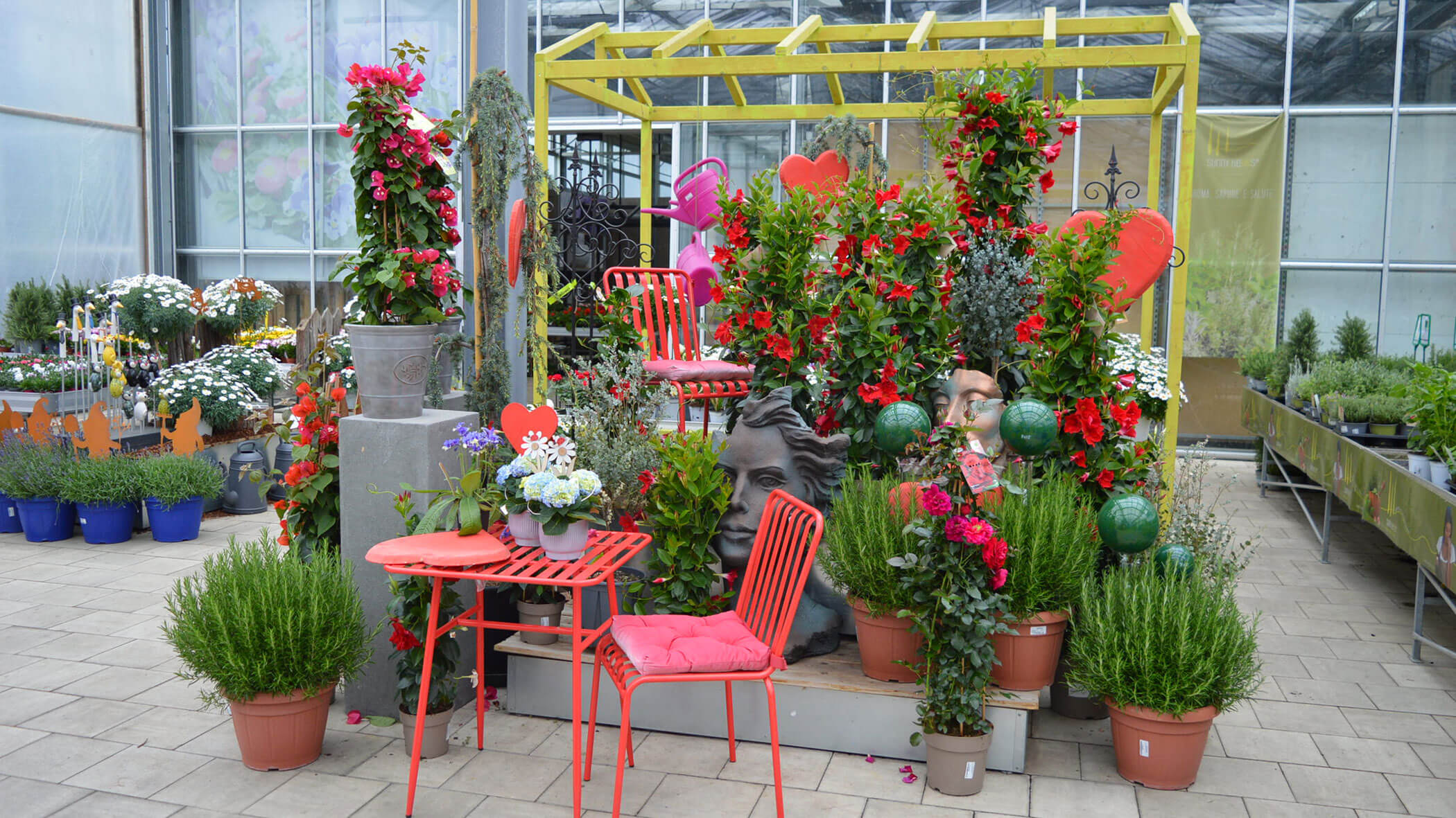 Eine farbenfrohe Gartencenter-Ausstellung mit roten Stühlen, Topfpflanzen, Blumen und dekorativen Herzformen. - Obojes