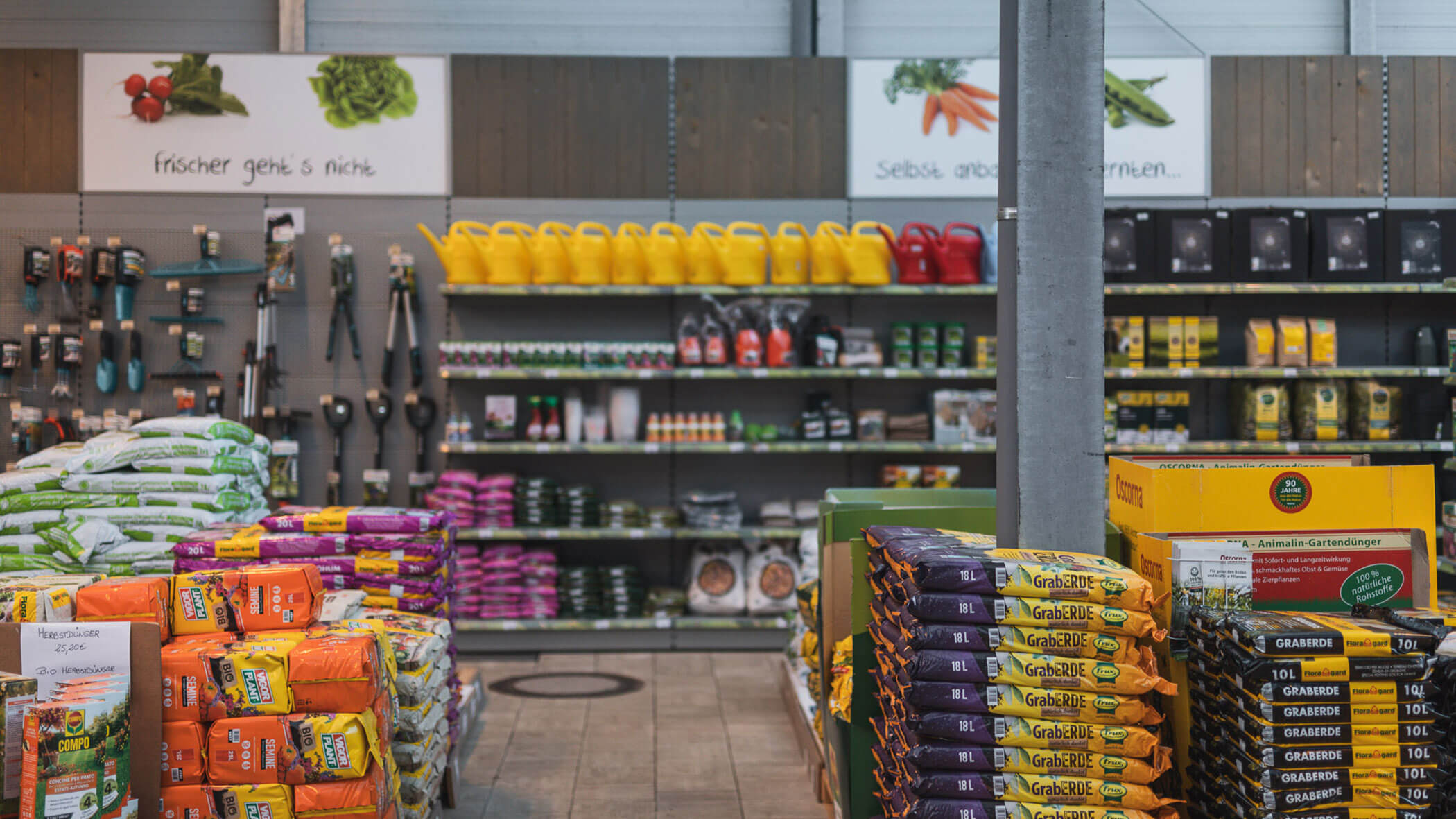 Ein Gang in einem Gartenbedarfsgeschäft mit Erdsäcken, Gießkannen und Gartengeräten in den Regalen. - Obojes