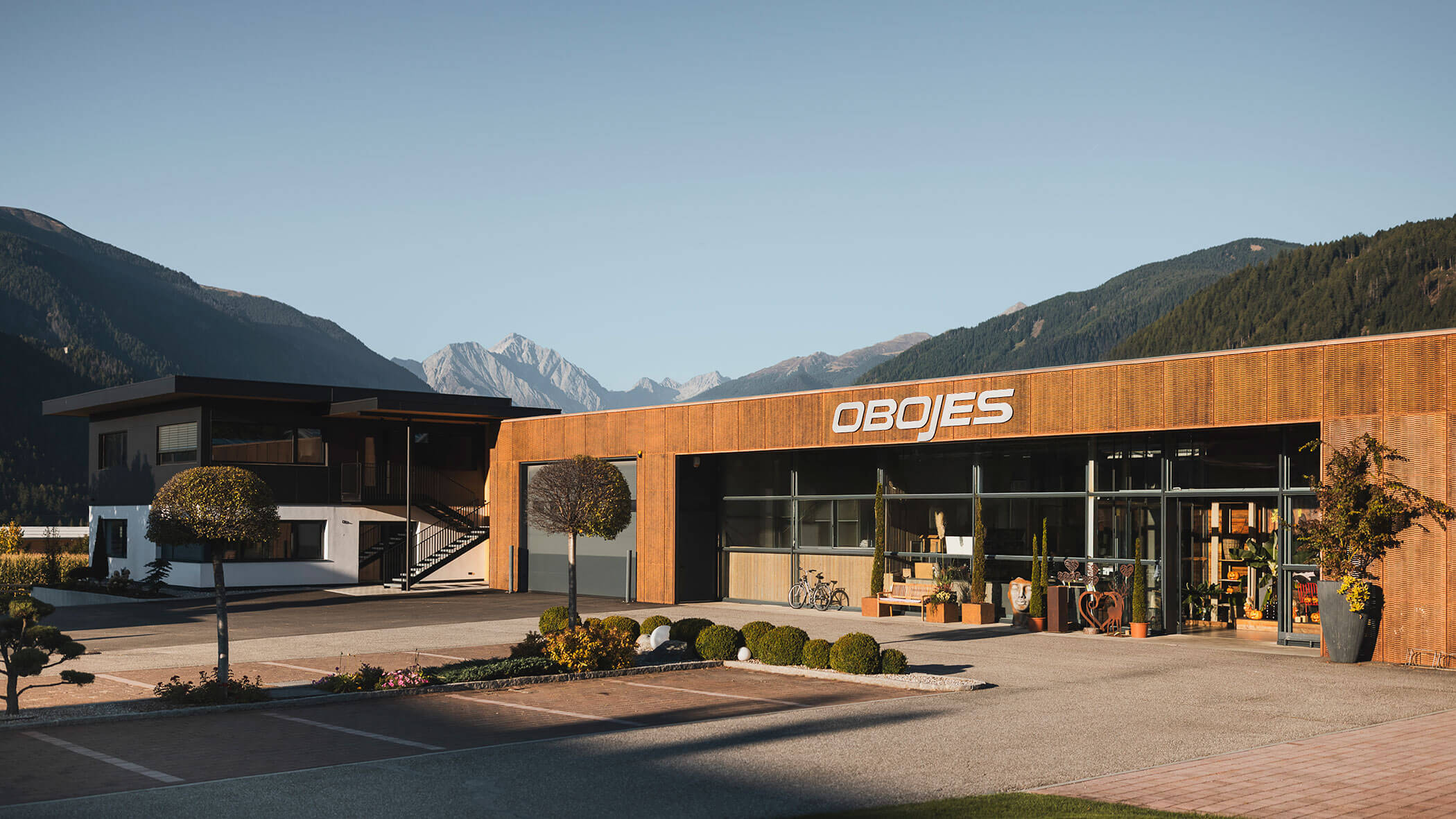 Modernes Gebäude mit OBOJES-Schild, umgeben von Bergen und Grün an einem klaren, sonnigen Tag. - Obojes