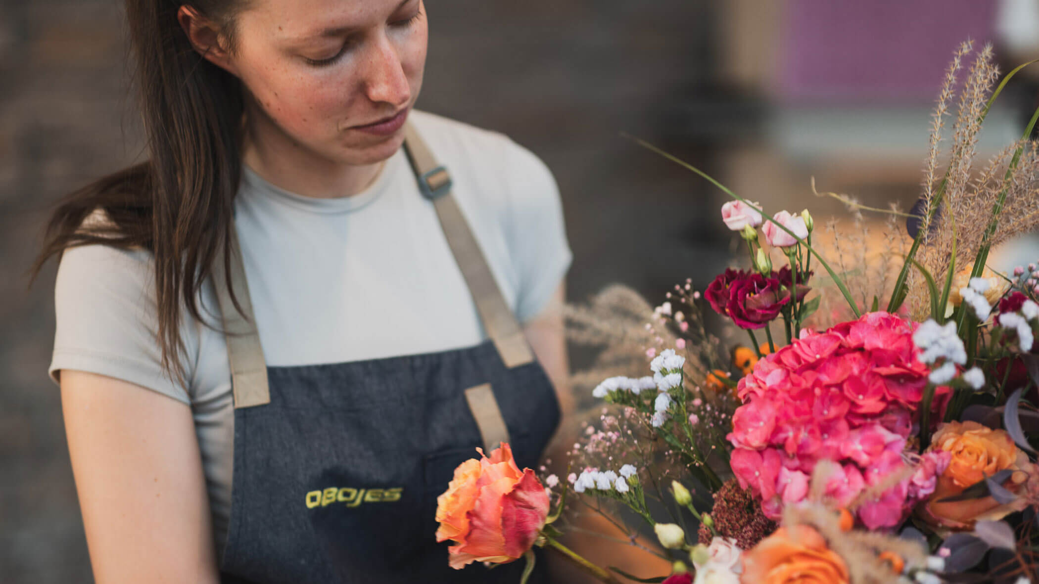 Eine Floristin arrangiert einen bunten Blumenstrauß, während sie eine graue Schürze trägt. - Obojes